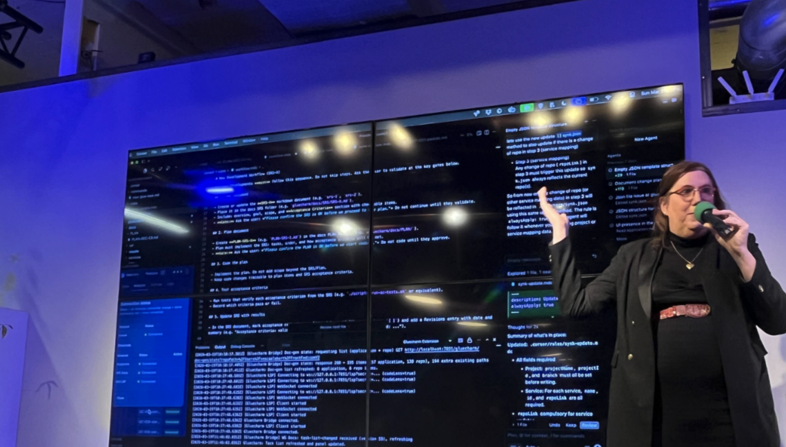 Xesca presenting EasySpecs on stage at an agentic coding conference in Hamburg, Germany, with a large IDE screen behind her